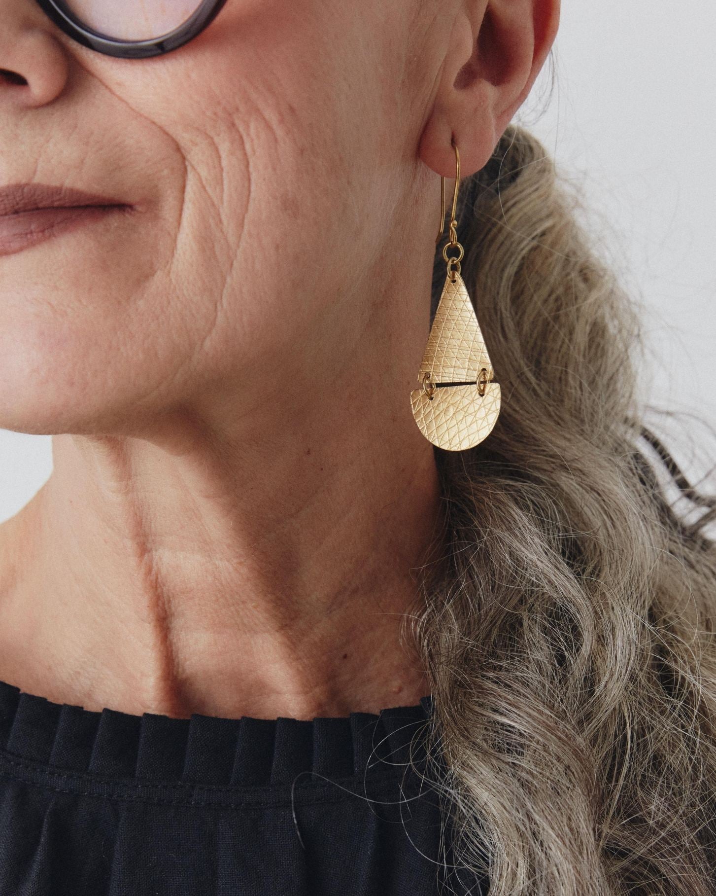Close-up of a person wearing gold teardrop earrings with a neutral background
