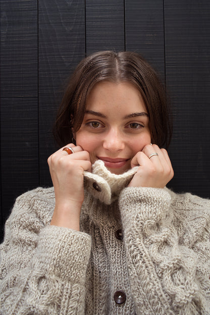 Woman wearing a beige knitted cardigan against a dark wooden background