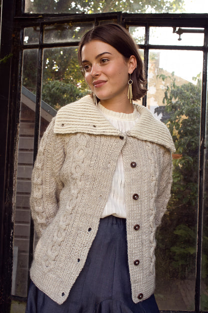 Woman wearing a beige knitted cardigan with buttons in front of a glass door.