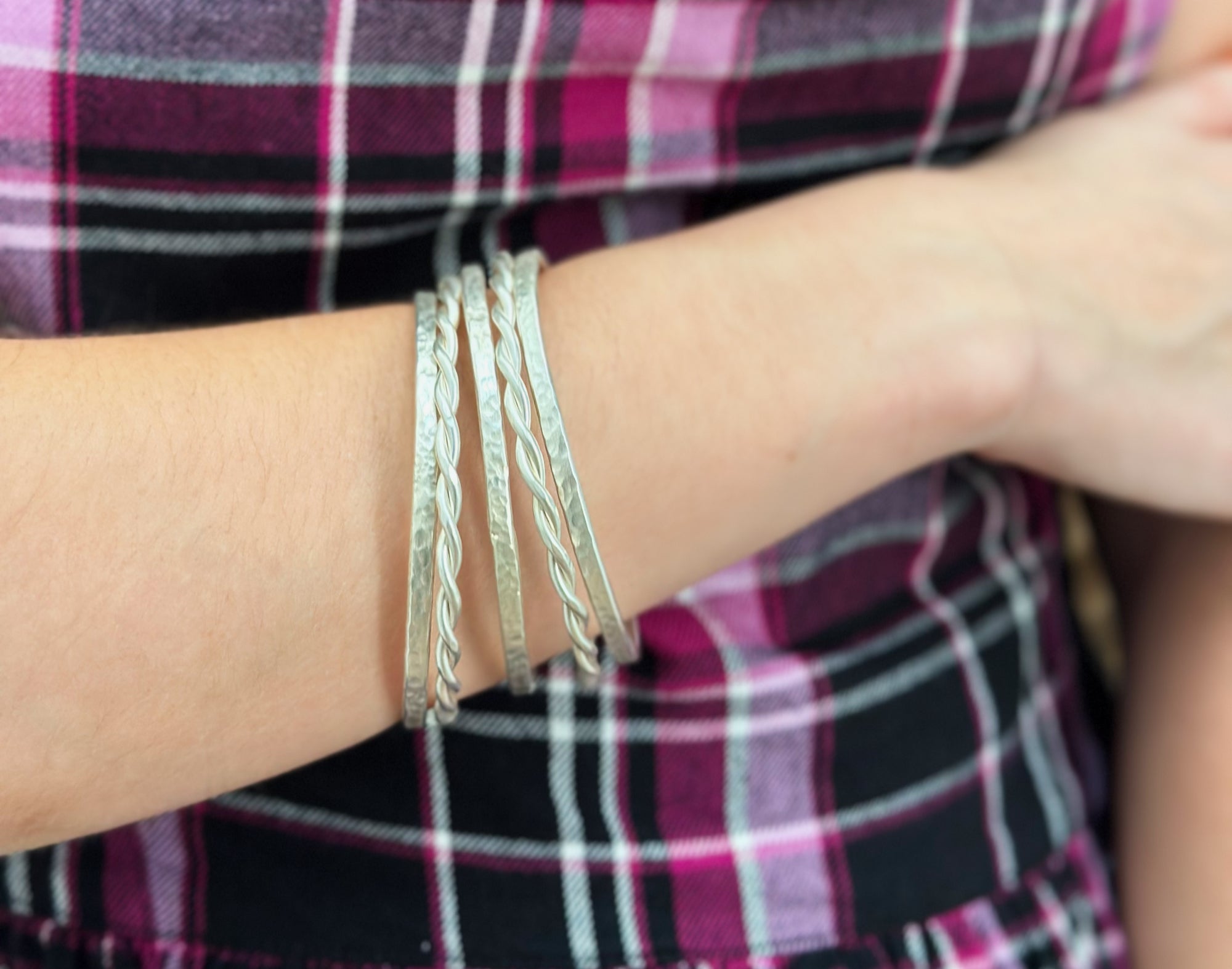 Silver bracelets on a wrist with a plaid shirt background