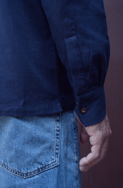 Person wearing a blue shirt and jeans against a dark background
