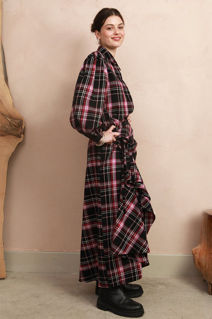 Side view of the berry and black check Rebel Skirt styled hitched up into a ruffled, asymmetrical drape, paired with a matching long-sleeve blouse and black boots