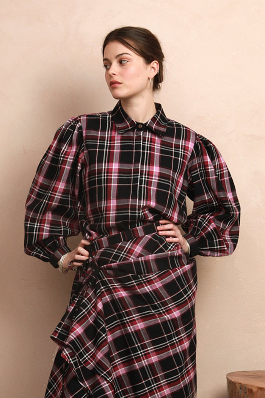 Full-length view of the berry and black check Rebel Skirt styled hitched up into a ruffled, asymmetrical drape, paired with a matching long-sleeve blouse and black boots