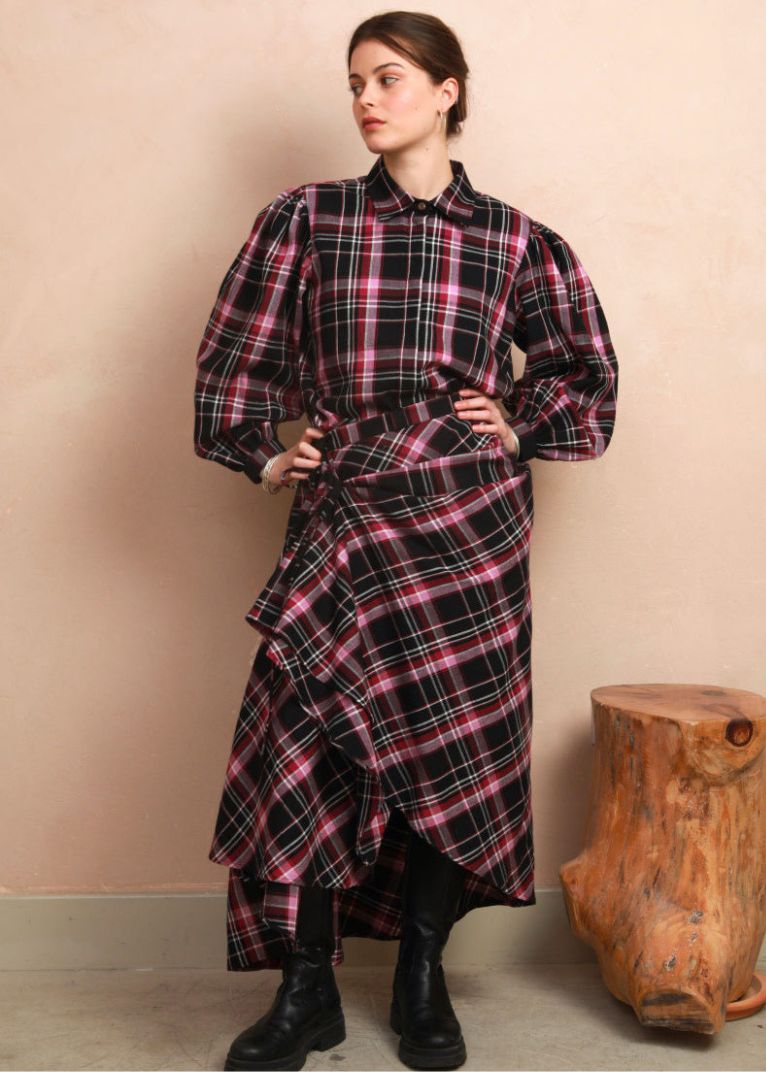 Full-length view of the berry and black check Rebel Skirt styled hitched up into a ruffled, asymmetrical drape, paired with a matching long-sleeve blouse and black boots