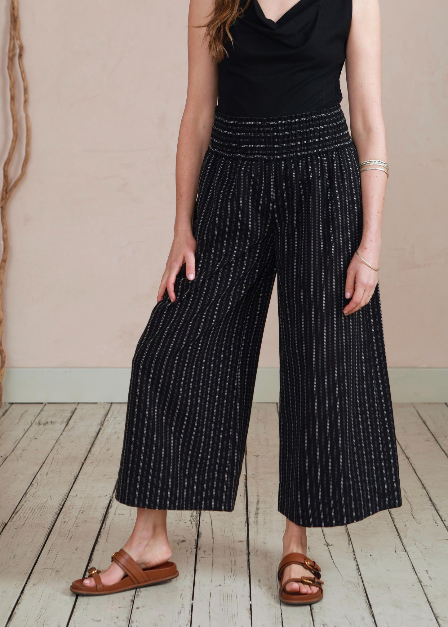 Woman wearing a black sleeveless top and wide-leg pants on a wooden floor.