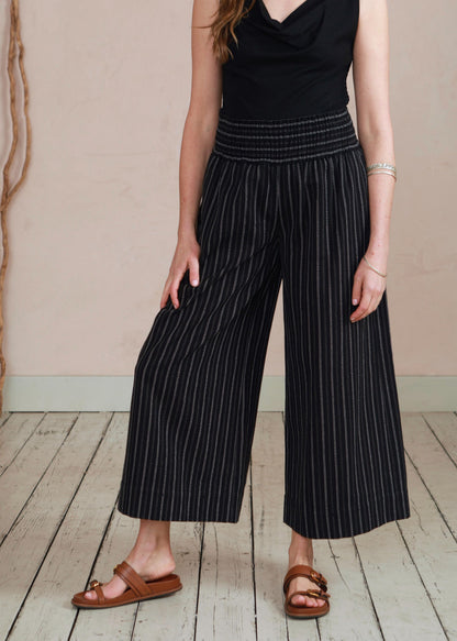Woman wearing a black sleeveless top and wide-leg pants on a wooden floor.