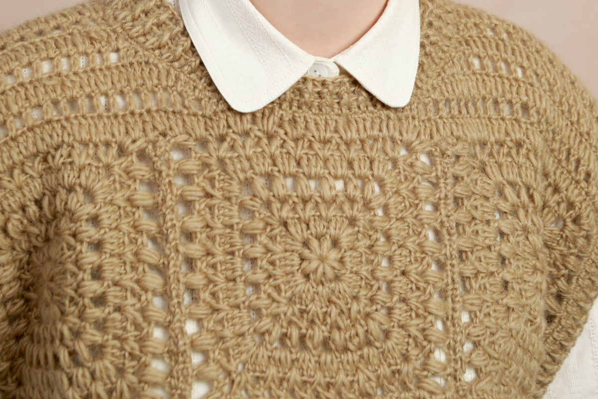 Close-up shot showing the geometric crochet square motif and collar detail on the natural corn yellow vest