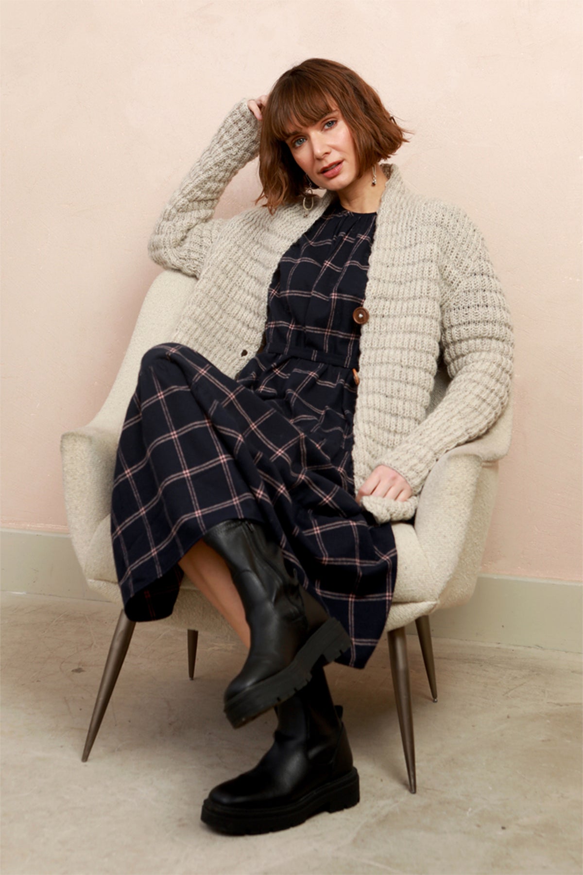 A woman wearing a navy blue plaid midi dress with long sleeves and a tiered skirt, sat down on chair