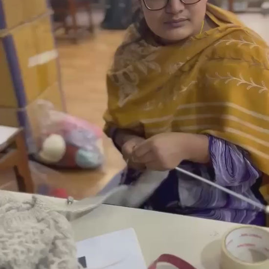 Artisan hand-knitting the natural charcoal grey basket stitch cardigan at Kumbheshwar Technical School