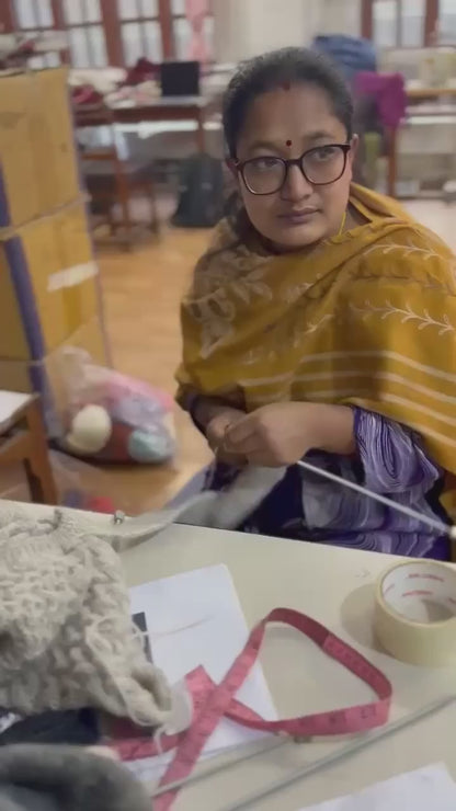 Artisan hand-knitting the natural charcoal grey basket stitch cardigan at Kumbheshwar Technical School