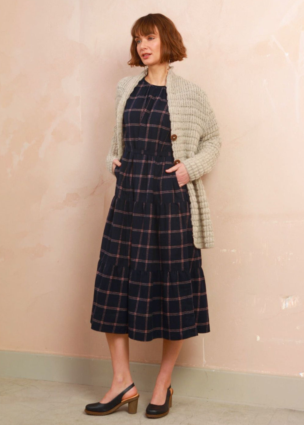 Model wearing the navy and pink check Roseby Dress styled with an cream knit cardigan layered over top