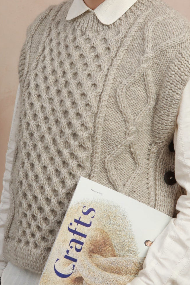 Close-up texture shot showing the intricate cable knit pattern and side-button details on the light grey slipover