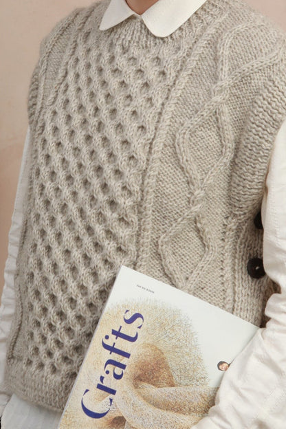 Close-up texture shot showing the intricate cable knit pattern and side-button details on the light grey slipover