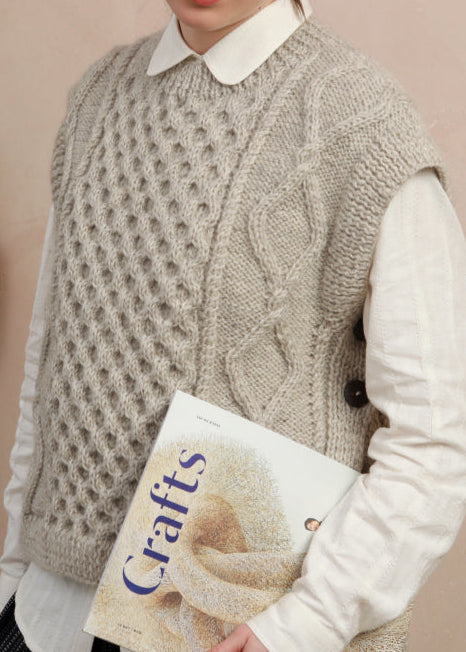 Close-up texture shot showing the intricate cable knit pattern and side-button details on the light grey slipover