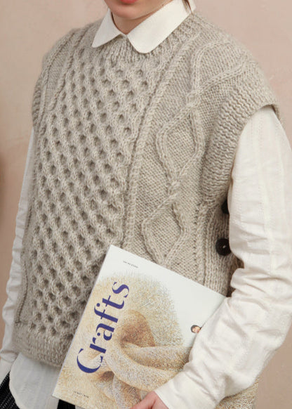 Close-up texture shot showing the intricate cable knit pattern and side-button details on the light grey slipover