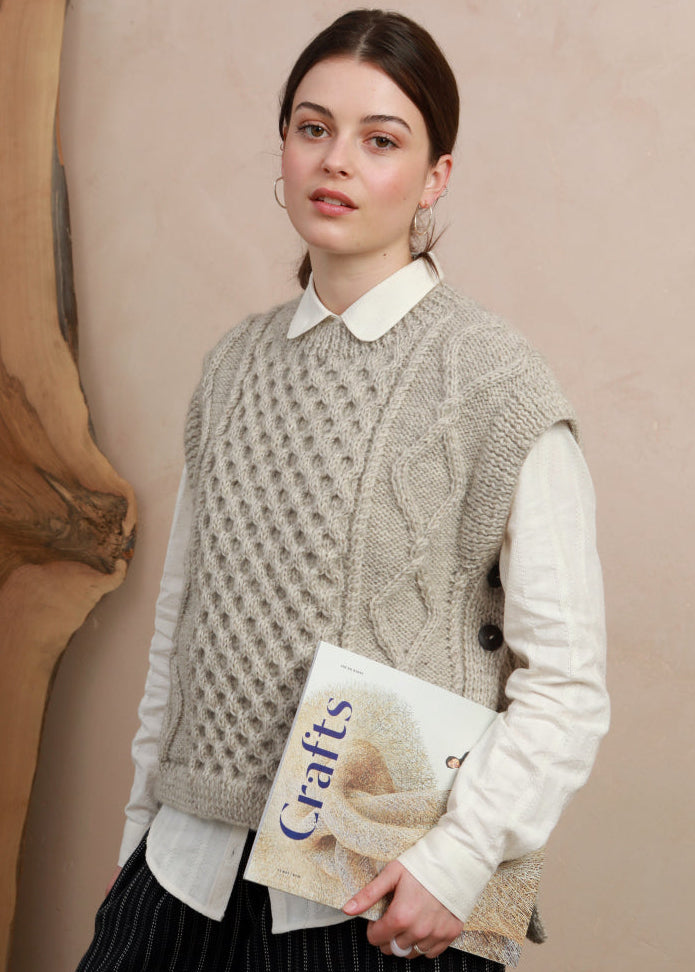 Model wearing the natural light grey hand-knit cable slipover vest layered over a white collared shirt