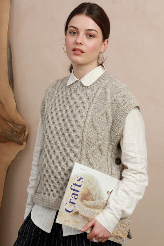 Model wearing the natural light grey hand-knit cable slipover vest layered over a white collared shirt