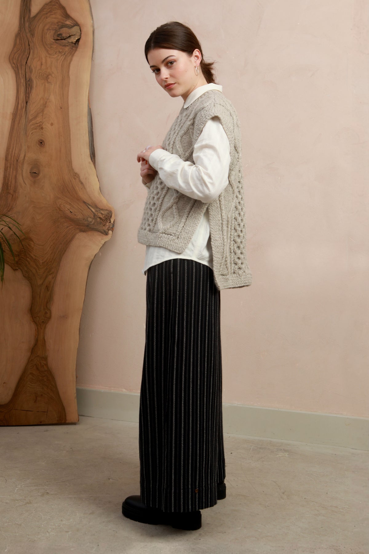 Side view of model wearing the natural light grey hand-knit slipover styled with wide-leg black trousers
