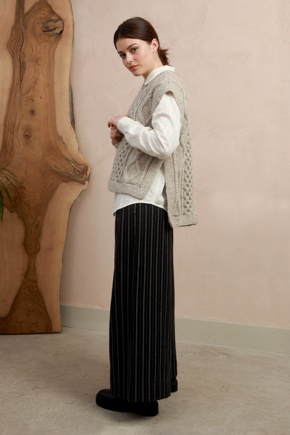 Side view of model wearing the natural light grey hand-knit slipover styled with wide-leg black trousers