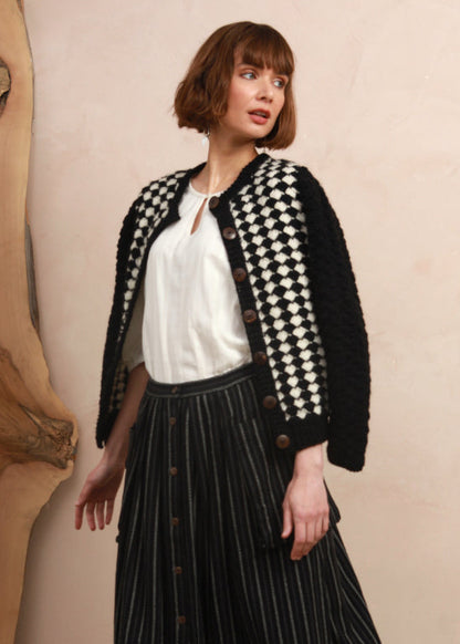 Three-quarter view of model in the two-tone hand-knit cardigan showing natural coconut shell button details