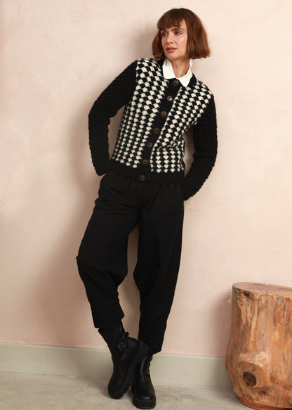 Full-length view of model wearing the black and white hand-knit cardigan styled with black trousers